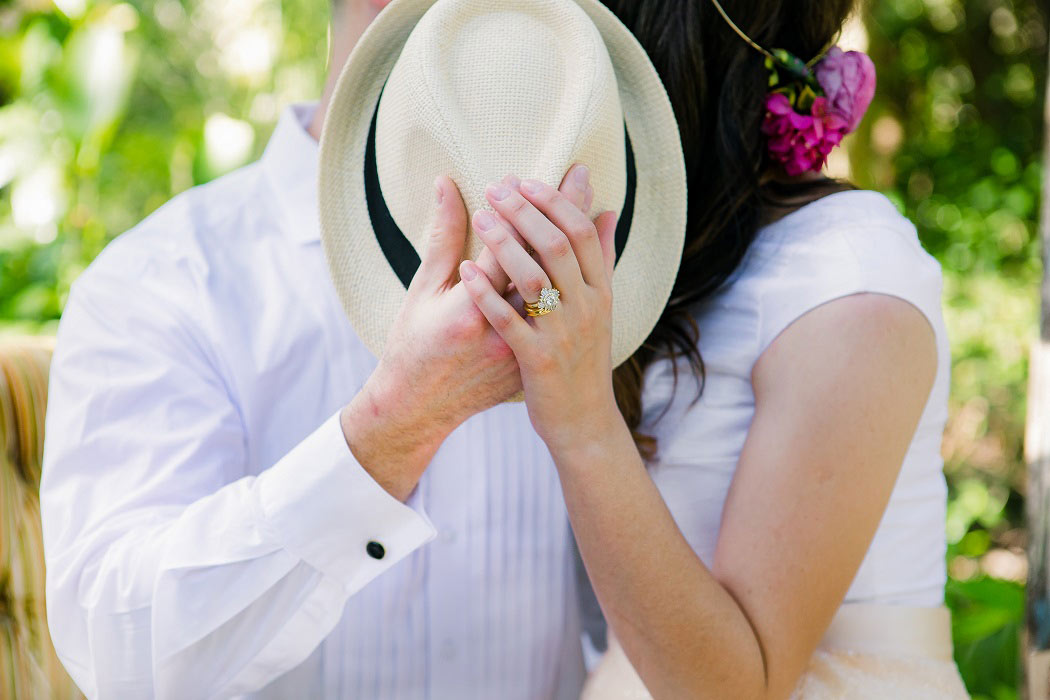 bride and groom kiss behind straw fedora