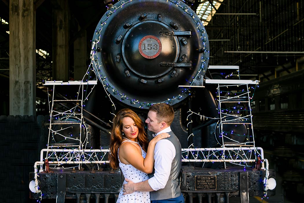 engaged couple posing in front of locomotive | vintage engagement session south florida | engagement session with trains miami