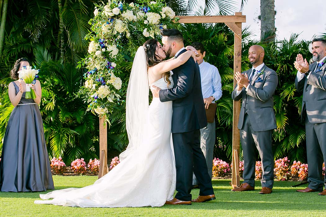 wooden arch with yellow and purple wedding flowers | bride and groom first kiss