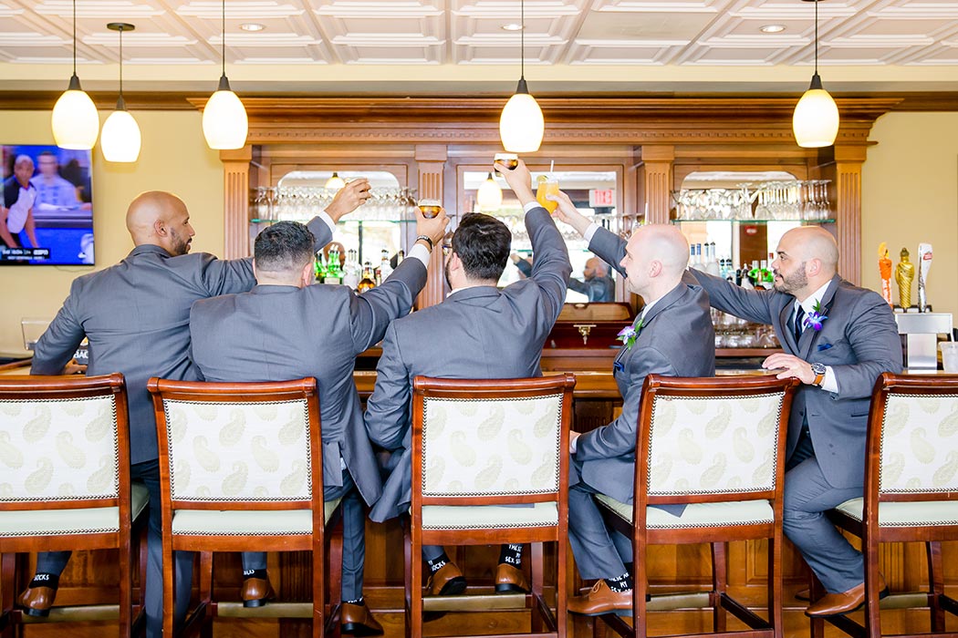 fun photograph with groom and groomsmen at bar | groom and groomsmen raising drink glasses at bar
