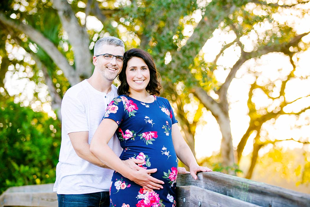 husband and wife maternity pose idea | pose for maternity photography with two people | tree tops park maternity photography | park maternity photoshoot with blue floral maternity dress