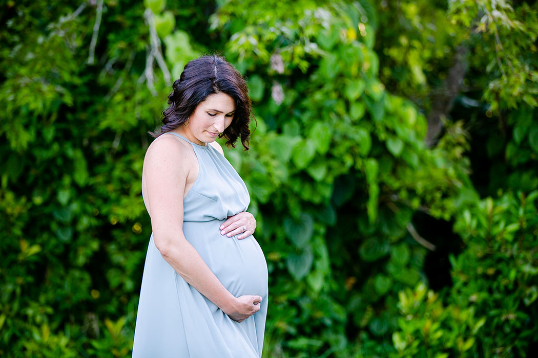 black haired woman in light green long maternity dress holds belly | expectant mother holds belly in photoshoot | maternity photographer south florida