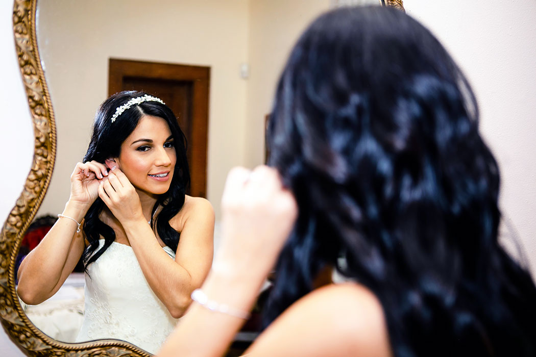 bride putting on earrings in front of a mirror at the historical society fort lauderdale