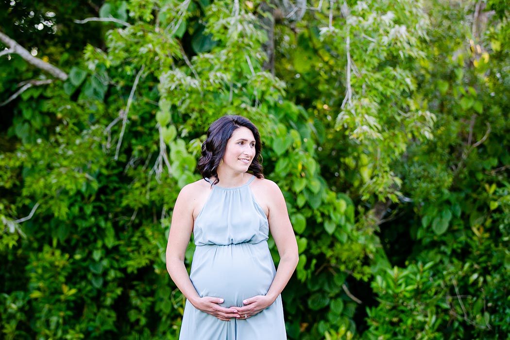 woman holds belly for maternity photography | maternity poses holding belly | light green long maternity dress with black hair | maternity session in park
