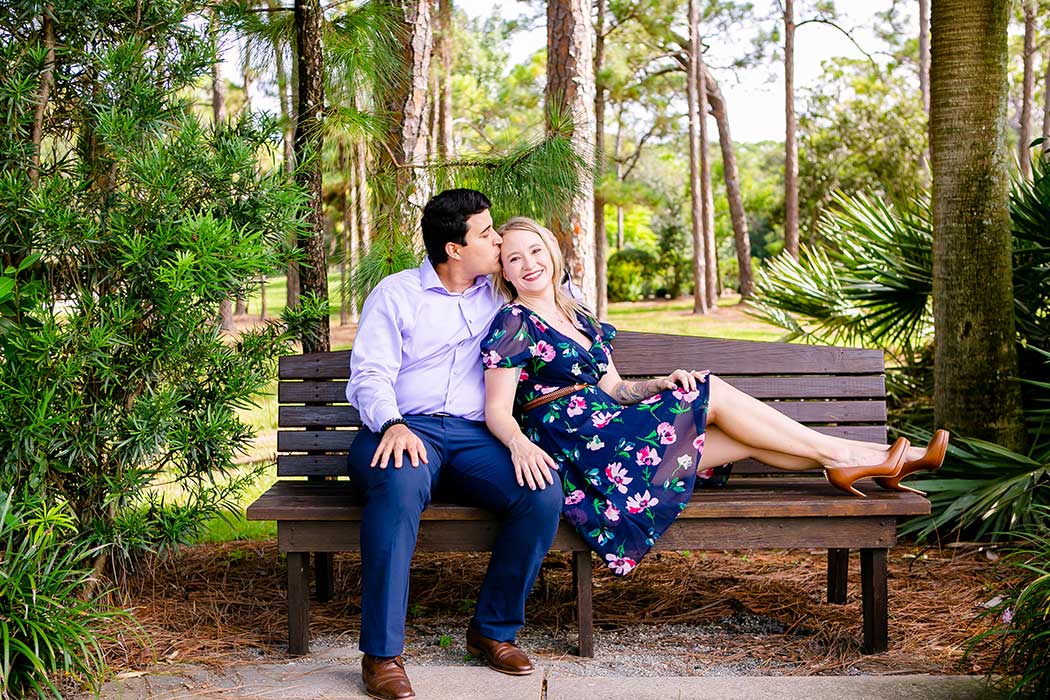 engagement pose sitting down | navy blue floral dress for engagement photoshoot | couple sit on bench for engagement session | engagement photoshoot at morikami japanese gardens                  