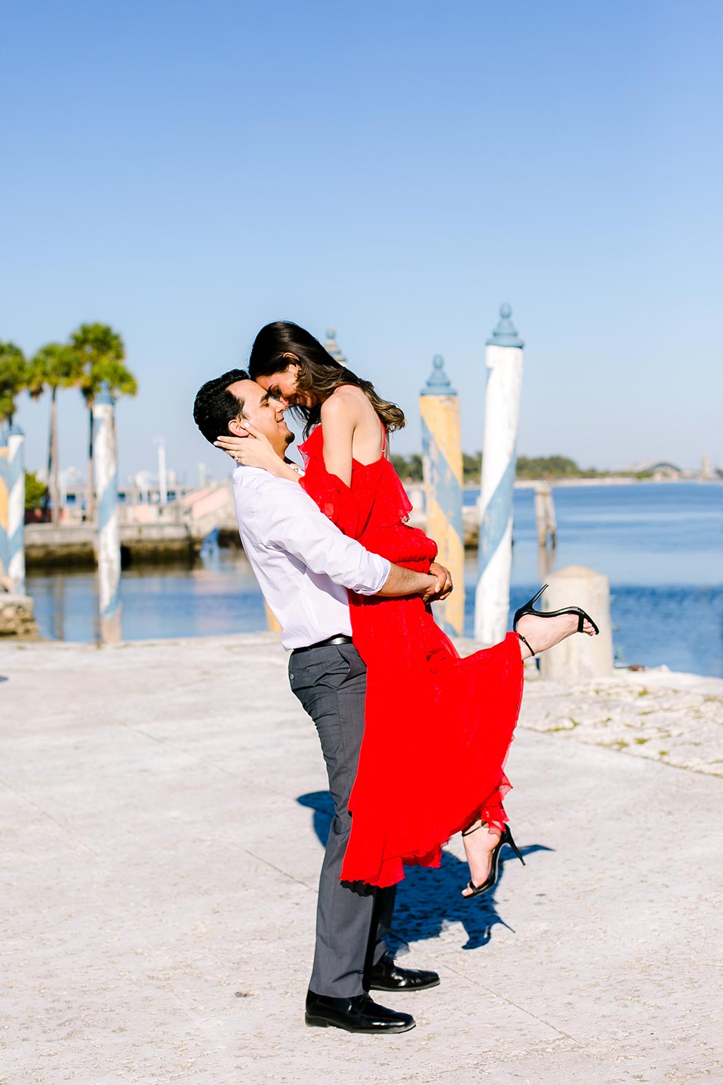 guy lifts girl in red dress near water at vizcaya | engagement photos vizcaya