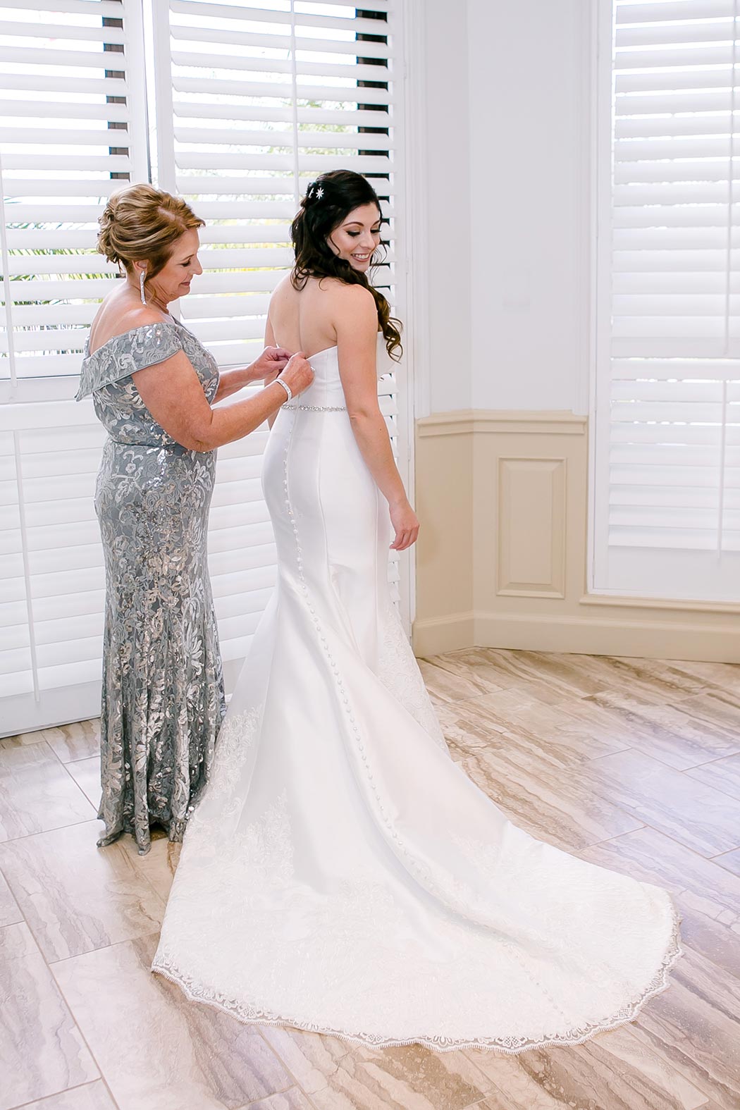 mom helping daughter getting into her bridal dress | mom fastening buttons on daughters bridal dress