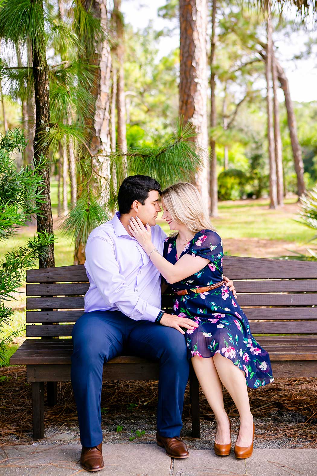 girl in navy floral dress poses for engagement photographs on wooden bench | morikami engagement photographs | engagement photography at morikami japanese gardens
