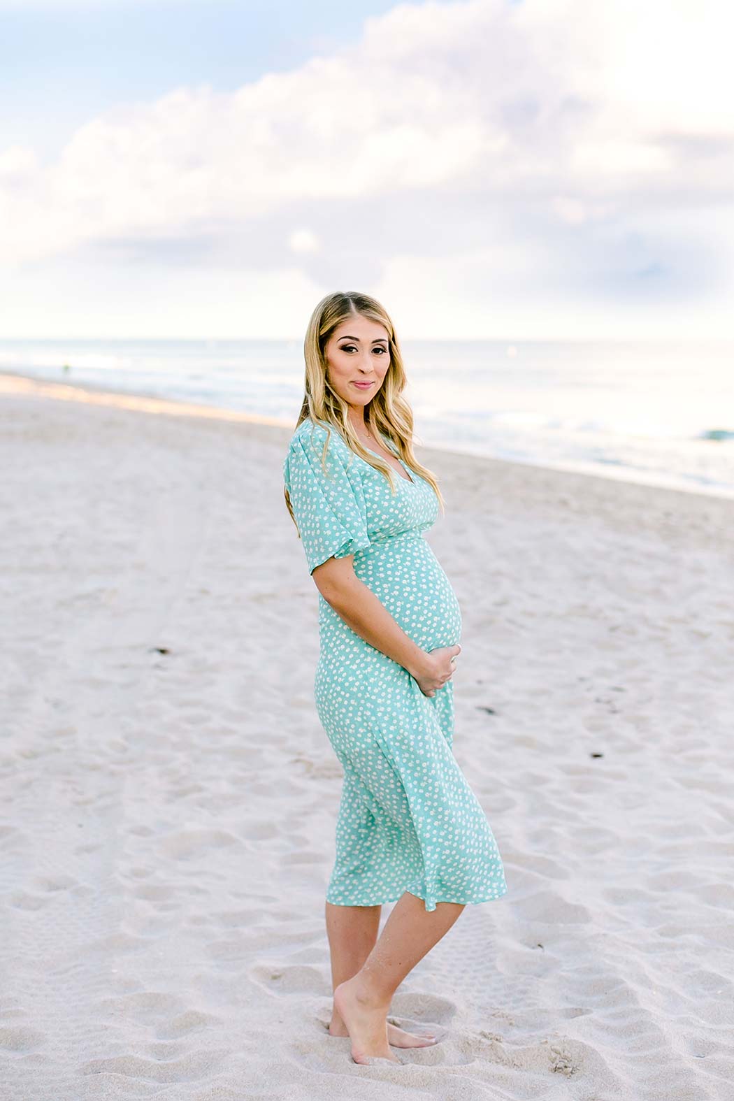 woman holds belly for maternity photography | maternity poses holding belly | light green long maternity dress | maternity session on fort lauderdale beach