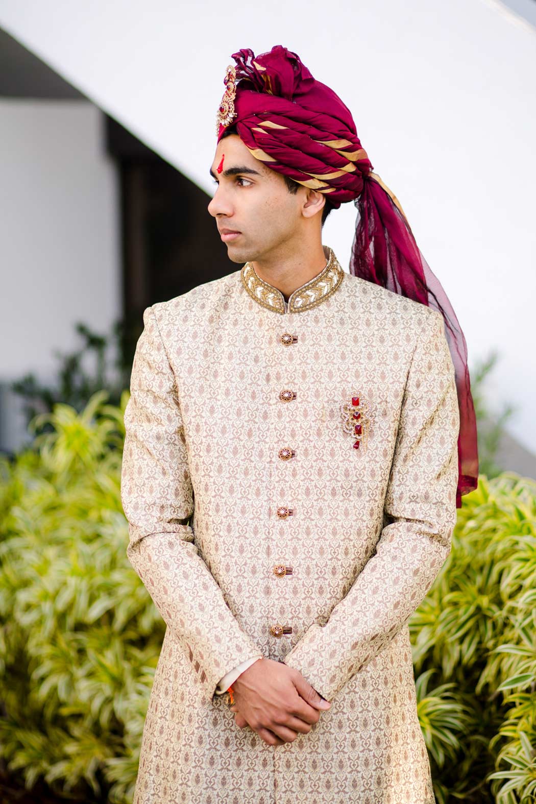 handsome south indian groom poses in traditional gold suit with red turban in south florida