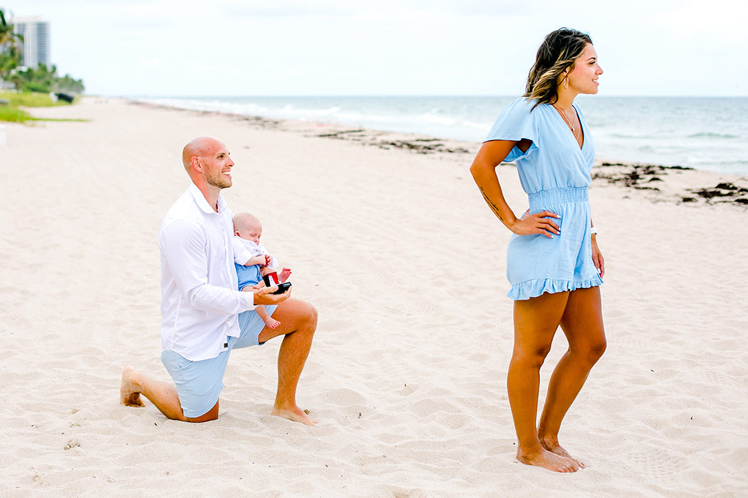 guy on one knee proposing on fort lauderdale beach | engagement photography fort lauderdale beach | proposal photography on beach with baby