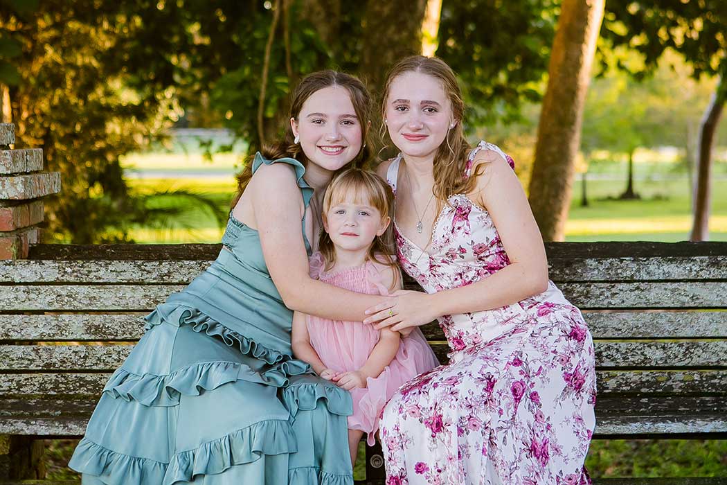 3 sisters pose on wooden bench in robbins preserve for family photoshoot