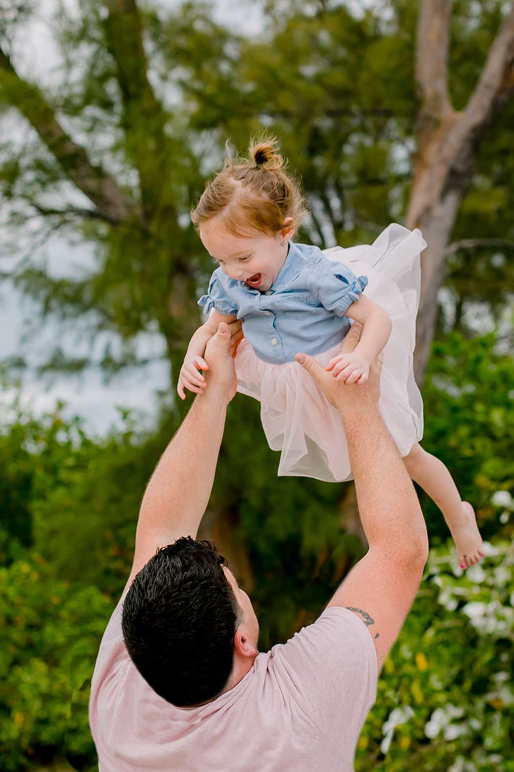 dad throws laughing young daughter in the air for family photososhoot