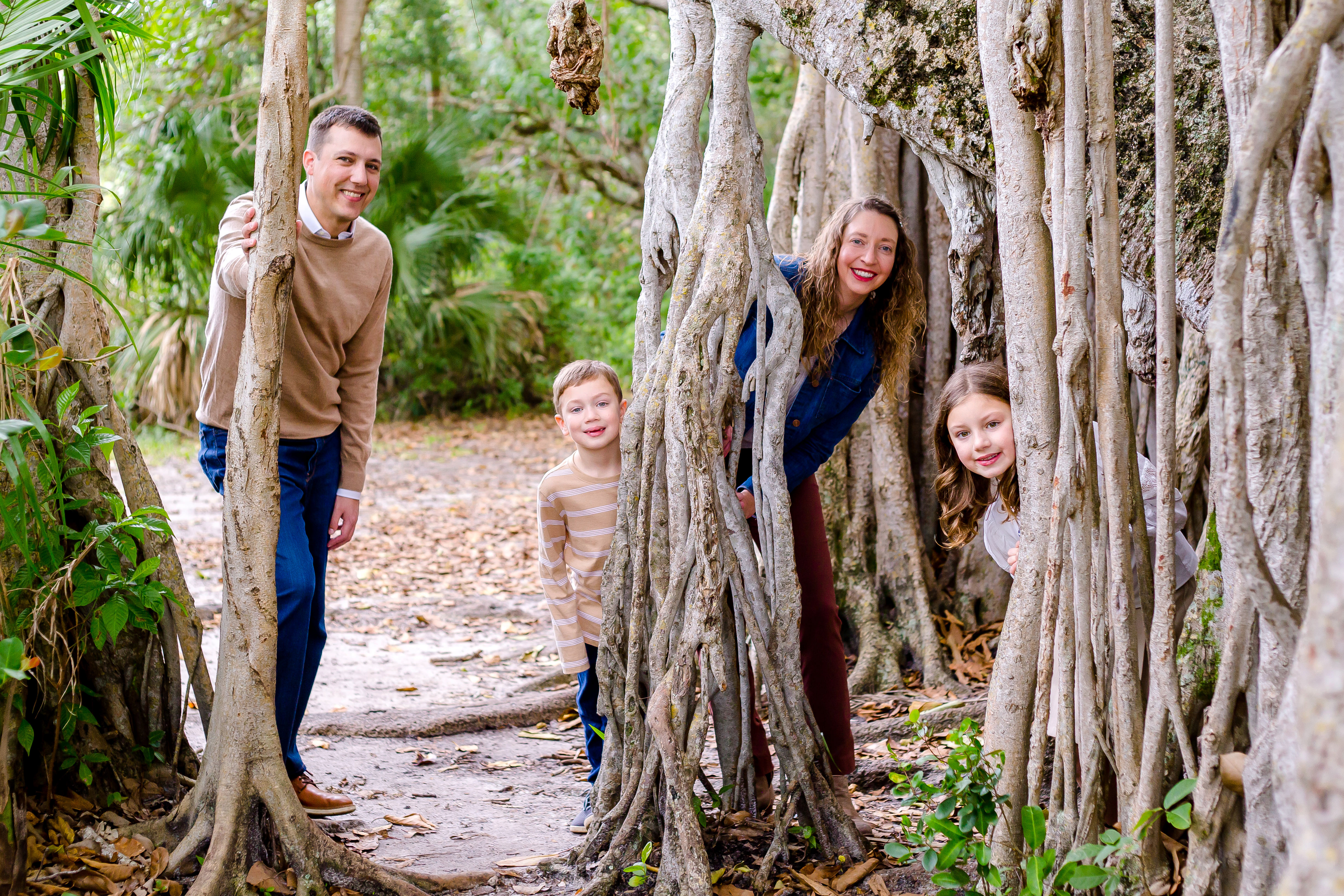 family of 4 peek around hammock tree for family photoshoot in robbins park