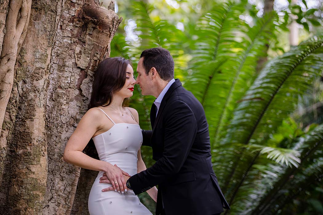 Outdoor couples photoshoot in Flamingo Gardens, featuring a couple surrounded by palm trees leaning against tree