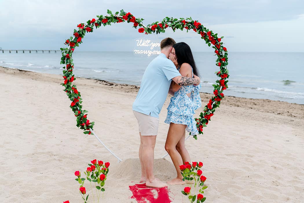 Romantic surprise proposal under a heart-shaped floral arch on Fort Lauderdale Beach