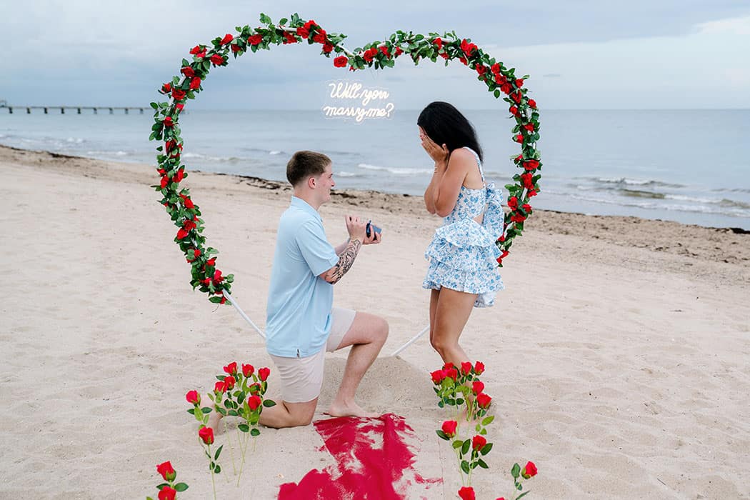 Guy proposing to his girlfriend under a heart-shaped floral arch on Fort Lauderdale Beach